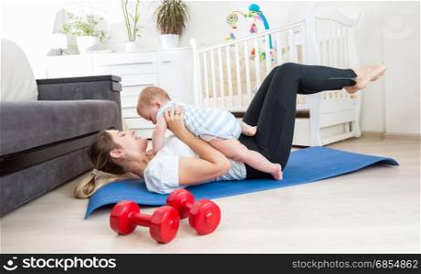Happy mother doing exercise at home and having fun with her baby boy