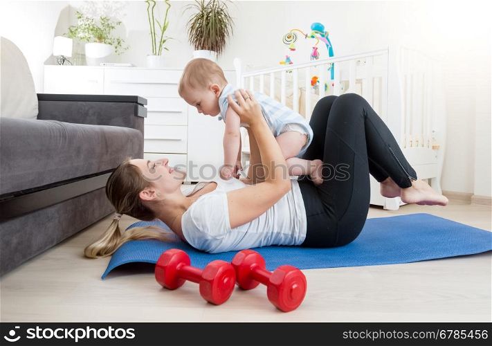 Happy mother doing yoga with her baby boy on floor at living room