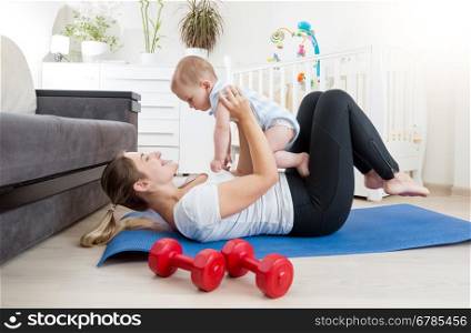 Happy mother doing yoga with her baby boy on floor at living room