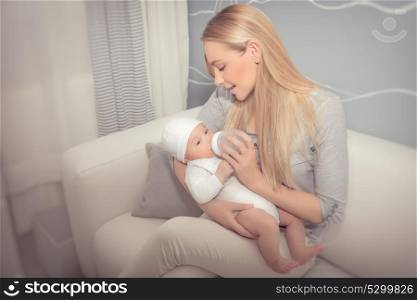Happy mother feeding her adorable newborn baby in the nice cozy kid&rsquo;s room at home, healthy milk nutrition for infants, enjoying parenthood