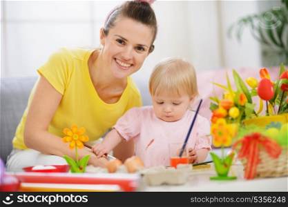 Happy mother helping baby painting on Easter eggs