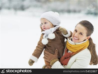 Happy mother holding baby looking on copy space in winter park