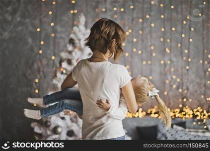 Happy mother holding her daughter in her arms on the background of Christmas decorations.. A young mother holding a happy child 7160.