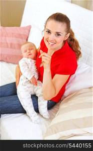 Happy mother holding sleeping baby and showing shhh gesture&#xA;
