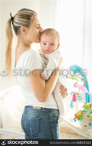 Happy mother hugging her 3 months old baby at big window in bedrrom