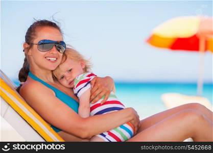 Happy mother laying on sun bed and hugging baby