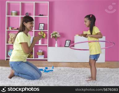 Happy mother looking at daughter spinning hula hoop at home