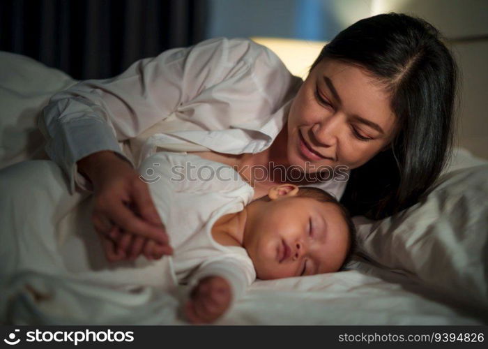 happy mother looking with her infant baby sleeping on a bed at night