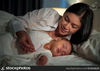 happy mother looking with her infant baby sleeping on a bed at night