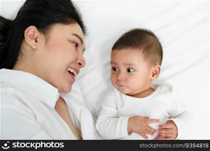 happy mother lying with her infant baby on a bed  top view 