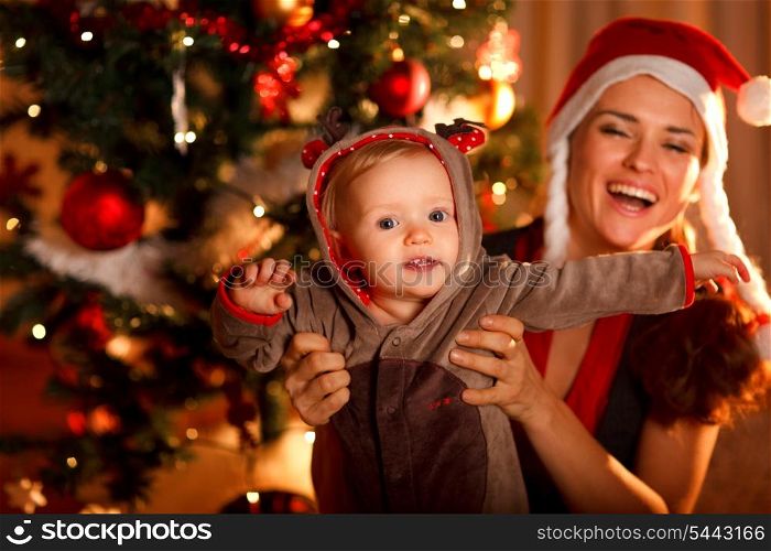 Happy mother playing with baby near Christmas tree&#xA;