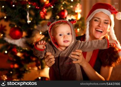 Happy mother playing with baby near Christmas tree&#xA;