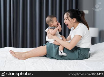 happy mother playing with baby on a bed at home