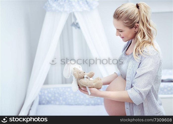 Happy mother prepares child&rsquo;s room, beautiful young pregnant woman with pleasure decorates bed of her future baby with toys, happy pregnancy concept