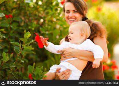 Happy mother showing flower to her baby on street&#xA;