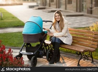Happy mother sitting on bench and looking at her baby in stroller