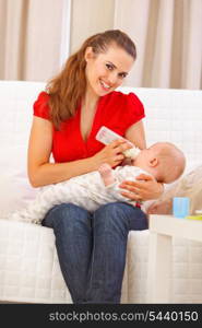 Happy mother sitting on couch and feeding baby