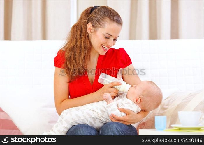 Happy mother sitting on sofa and feeding baby&#xA;