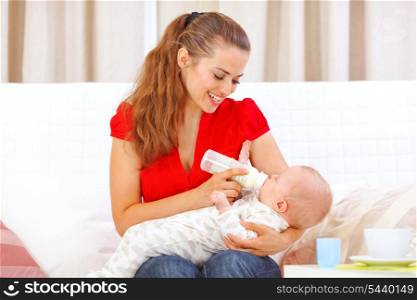 Happy mother sitting on sofa and feeding baby&#xA;