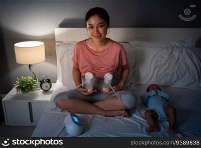 happy mother using breast pump machine to pumping milk with her newborn baby on a bed at night