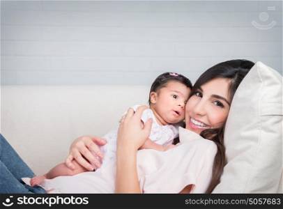 Happy mother with baby lying down on the couch at home, cheerful woman playing with her adorable daughter, love and happiness concept