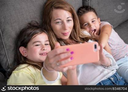 Happy mother with her kids are making a selfie or video call to father or relatives in a sofa. Concept of technology, new generation, family, connection, parenthood. High quality 4k footage. Happy mother with her kids are making a selfie or video call to father or relatives in a sofa. Concept of technology, new generation, family, connection, parenthood.