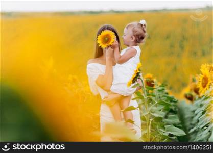 Happy mother with the daughter in the field with sunflowers. mom and baby girl having fun outdoors. family concept.mothers Day.. Happy mother with the daughter in the field with sunflowers. mom and baby girl having fun outdoors. family concept. mothers Day