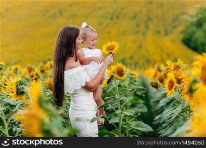 Happy mother with the daughter in the field with sunflowers. mom and baby girl having fun outdoors. family concept. mother&rsquo;s day.. Happy mother with the daughter in the field with sunflowers. mom and baby girl having fun outdoors. family concept. mother&rsquo;s day