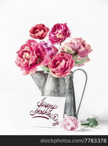 Happy mothers day greeting with pink peonies flowers bouquet in pitcher with greeting card and letters on white background. Celebrating with beautiful flowers bunch. Front view.