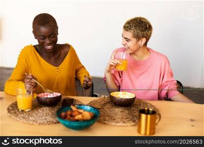 Happy multiethnic female couple relaxing at home while having breakfast. Happy young multiethnic female couple relaxing at home while having breakfast