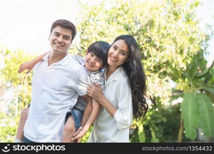 Happy multiracial caucasian asian family man piggyback little boy and mom hug from back standing outdoor yard on vacation summer,family have leisure picnic time together.