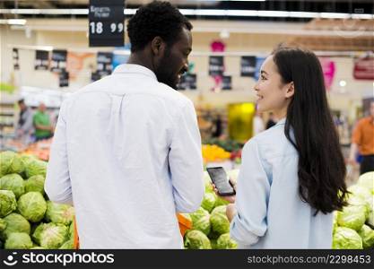 happy multiracial pair choosing goods supermarket
