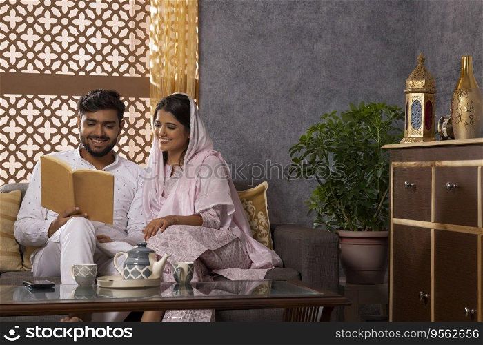 Happy Muslim couple reading a book together in living room