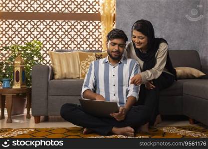 Happy Muslim couple using laptop in living room