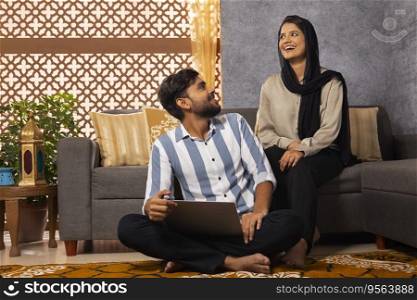 Happy Muslim couple using laptop in living room