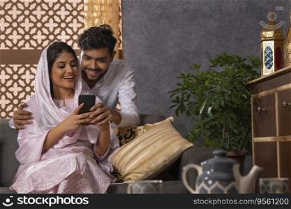 Happy Muslim couple using mobile together in living room