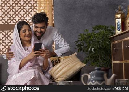 Happy Muslim couple using mobile together in living room