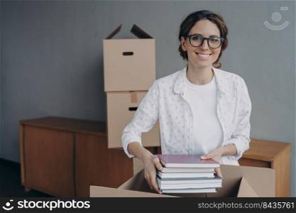 Happy nerd in glasses is stacking books into boxes. Young spanish woman packing carton container and puts textbooks and notebooks. Moving to rental apartment. Independence and entering to university.. Happy nerd in glasses is stacking books into boxes. Young spanish woman packing carton container.