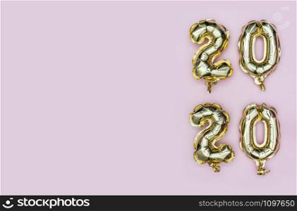 Happy New Year 2020. Vertical composition of number 2020 golden foil balloons on pastel pink background. Flat lay with copy space.. New Year 2020. Vertical composition of number 2020 golden foil balloons on pastel pink background. Flat lay with copy space.