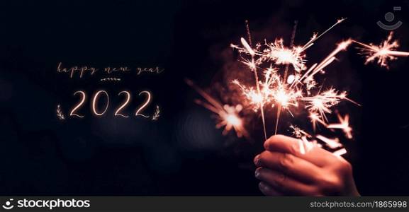 happy new year 2022 text with hand holding burning Sparkler firework blast with on a black bokeh background at night,holiday celebration event party,dark vintage tone