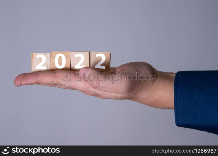 Happy New Year 2022 theme men&rsquo;s hands holding wooden cubes with the number 2022 on the palm. The concept of the new 2022.. Happy New Year 2022 theme men&rsquo;s hands holding wooden cubes with the number 2022 on the palm.