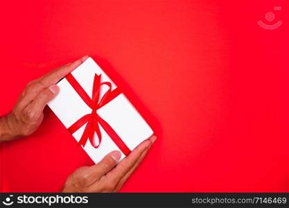 Happy New Year and Christmas 2020 or valentine day, top view hands with white gift box on red background with copy space for your text
