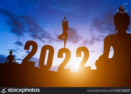 Happy New Year Numbers 2022, Silhouette Buddha statue and Silhouette woman practicing yoga early morning sunrise over the horizon background,Happy new year concept.