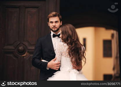 Happy newlywed couple hugging and kissing in old European town street, gorgeous bride in white wedding dress together with handsome groom. wedding day.. Happy newlywed couple hugging and kissing in old European town street, gorgeous bride in white wedding dress together with handsome groom. wedding day