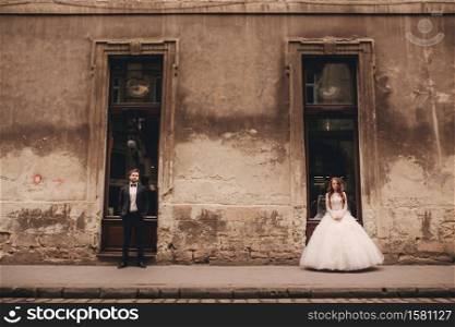 Happy newlywed couple on a walk in old European town street, gorgeous bride in white wedding dress together with handsome groom.. Happy newlywed couple on a walk in old European town street, gorgeous bride in white wedding dress together with handsome groom