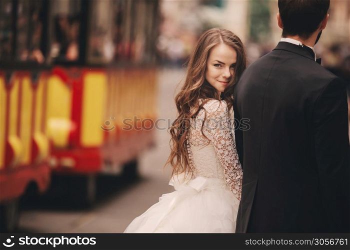 Happy newlyweds couple on a walk in old European town street, gorgeous bride in white wedding dress together with handsome groom. Happy newlyweds couple on a walk in old European town street, gorgeous bride in white wedding dress together with handsome groom.