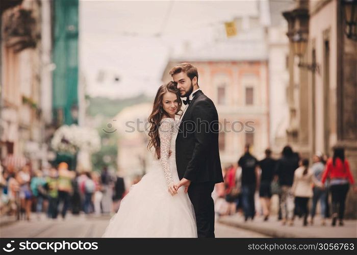 Happy newlyweds couple on a walk in old European town street, gorgeous bride in white wedding dress together with handsome groom. Happy newlyweds couple on a walk in old European town street, gorgeous bride in white wedding dress together with handsome groom.