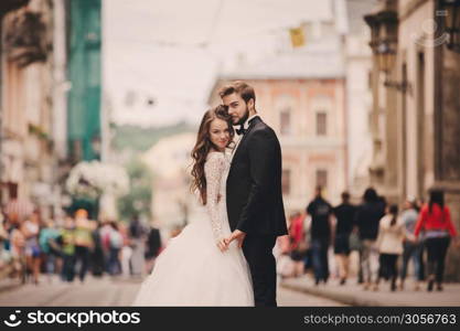 Happy newlyweds couple on a walk in old European town street, gorgeous bride in white wedding dress together with handsome groom. Happy newlyweds couple on a walk in old European town street, gorgeous bride in white wedding dress together with handsome groom.