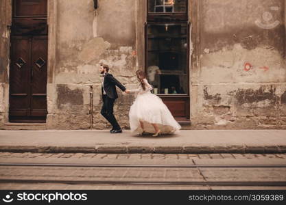 Happy newlyweds couple on a walk in old European town street, gorgeous bride in white wedding dress together with handsome groom. Happy newlyweds couple on a walk in old European town street, gorgeous bride in white wedding dress together with handsome groom.