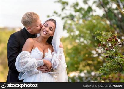 Happy newlyweds hug against the backdrop of a beautiful mountain landscape, the guy kisses the girl